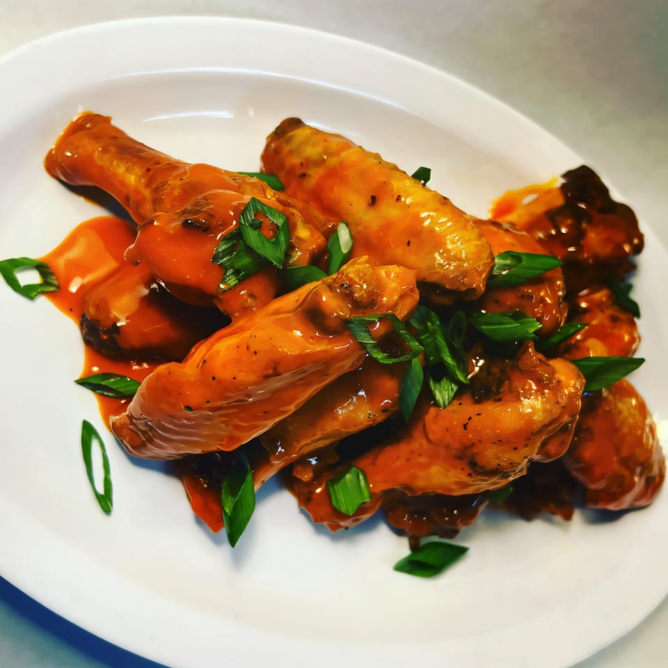 Mike's Gourmet Deli and Bagels' buffalo wings, coated in orange sauce and garnished with green onions.