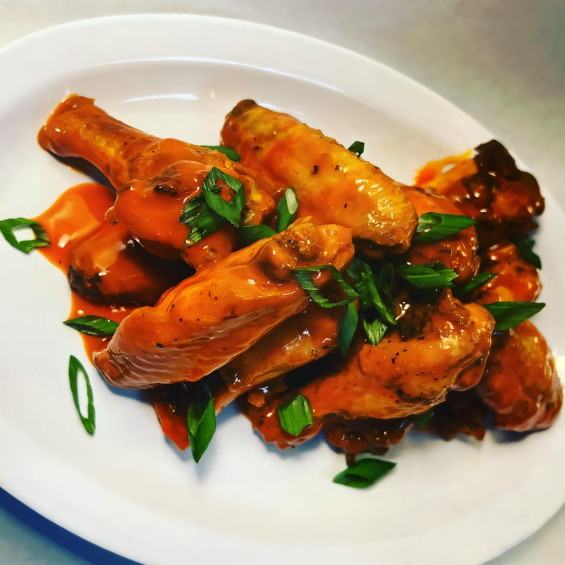 Mike's Gourmet Deli and Bagels' buffalo wings, coated in orange sauce and garnished with green onions.