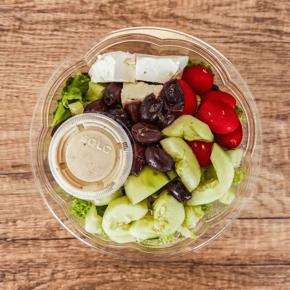 A Greek salad with lettuce, feta, olives, tomatoes, and cucumbers in a plastic container.