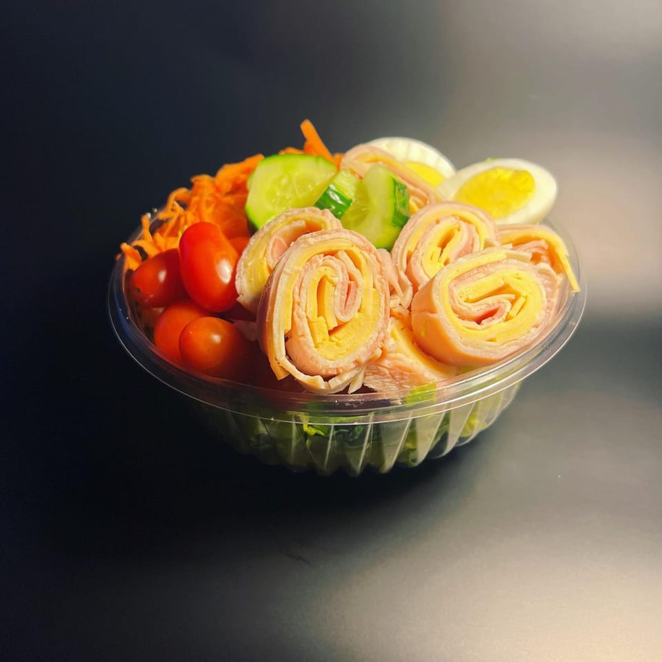 Deli salad with ham and cheese roll-ups, cherry tomatoes, shredded carrots, cucumbers, and hard-boiled eggs.